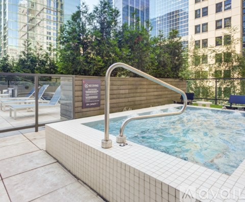 A hot tub sits on a tiled patio with a pool table and chairs in the background.