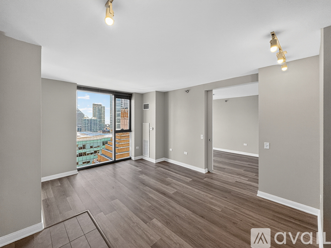 A spacious room with wooden flooring and a large window overlooking a cityscape.