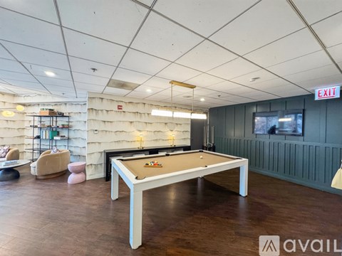 A pool table is in the middle of a room with a white ceiling and a TV on the wall.