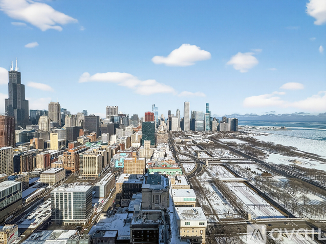 A cityscape with a mix of modern and older buildings, some snow on the ground, and a body of water in the distance.