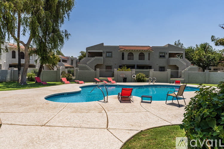 A swimming pool surrounded by a concrete patio and red chairs in front of a two-story house.