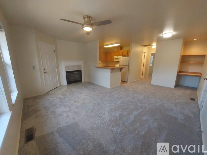A spacious living room with a ceiling fan and a kitchenette in the background.