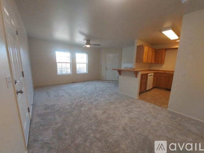 A spacious room with a carpeted floor, a ceiling fan, and a window with blinds.