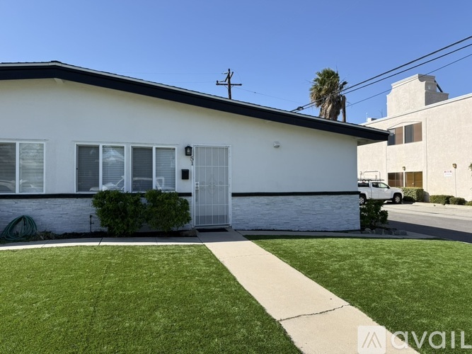 A white house with a black roof and a green bush in front.