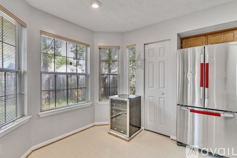 A kitchen with a stainless steel refrigerator and a window with blinds.