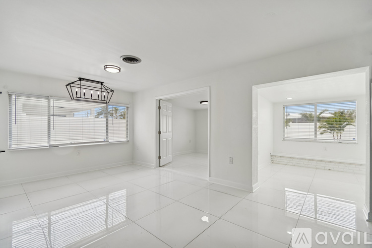 A spacious room with white walls and floor, a ceiling light, and a window with blinds.