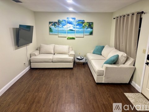 A living room with a white couch and a painting of a beach scene on the wall.