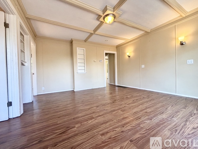 A spacious room with wooden flooring and white walls.