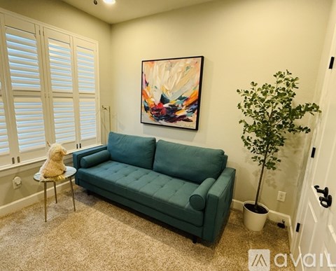 A living room with a green couch, a small table with a dog, a painting, and a plant.