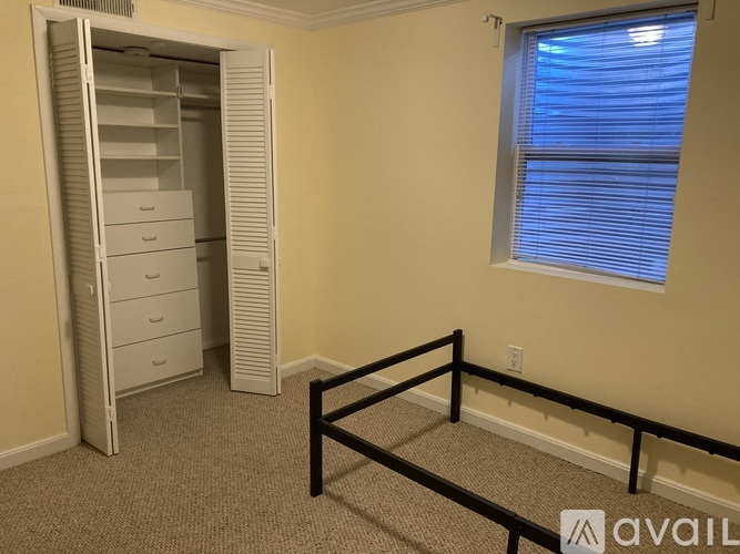 A room with a white closet, a window with blinds, and a carpeted floor.