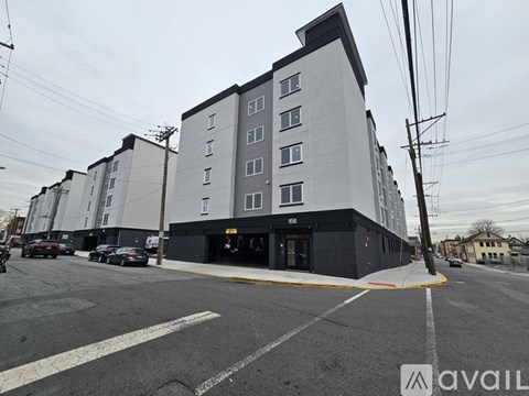 A street view of a large white building with a black roof and a parking lot in front.