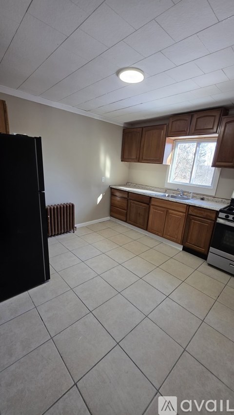 A kitchen with a black refrigerator, white tiled floor, and wooden cabinets.