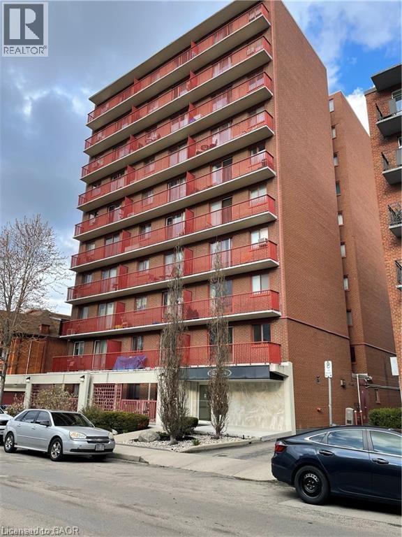 A tall red brick apartment building with cars parked in front.