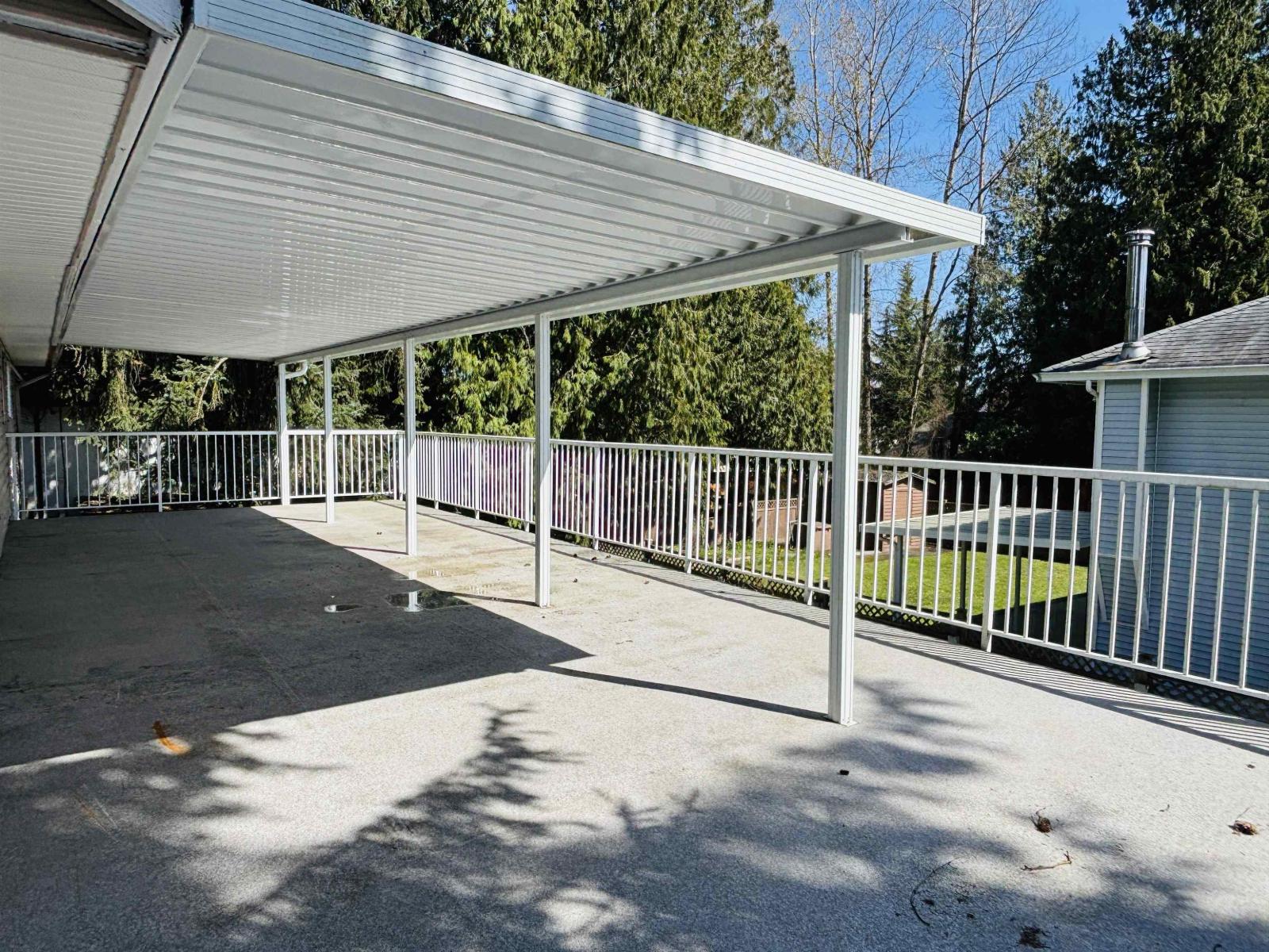 A covered patio area with a metal railing and a concrete floor.