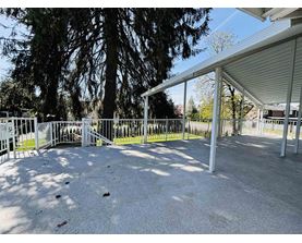 A white metal fence surrounds a gravel area with a large tree in the background.