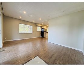 A spacious room with wooden flooring and a large window.