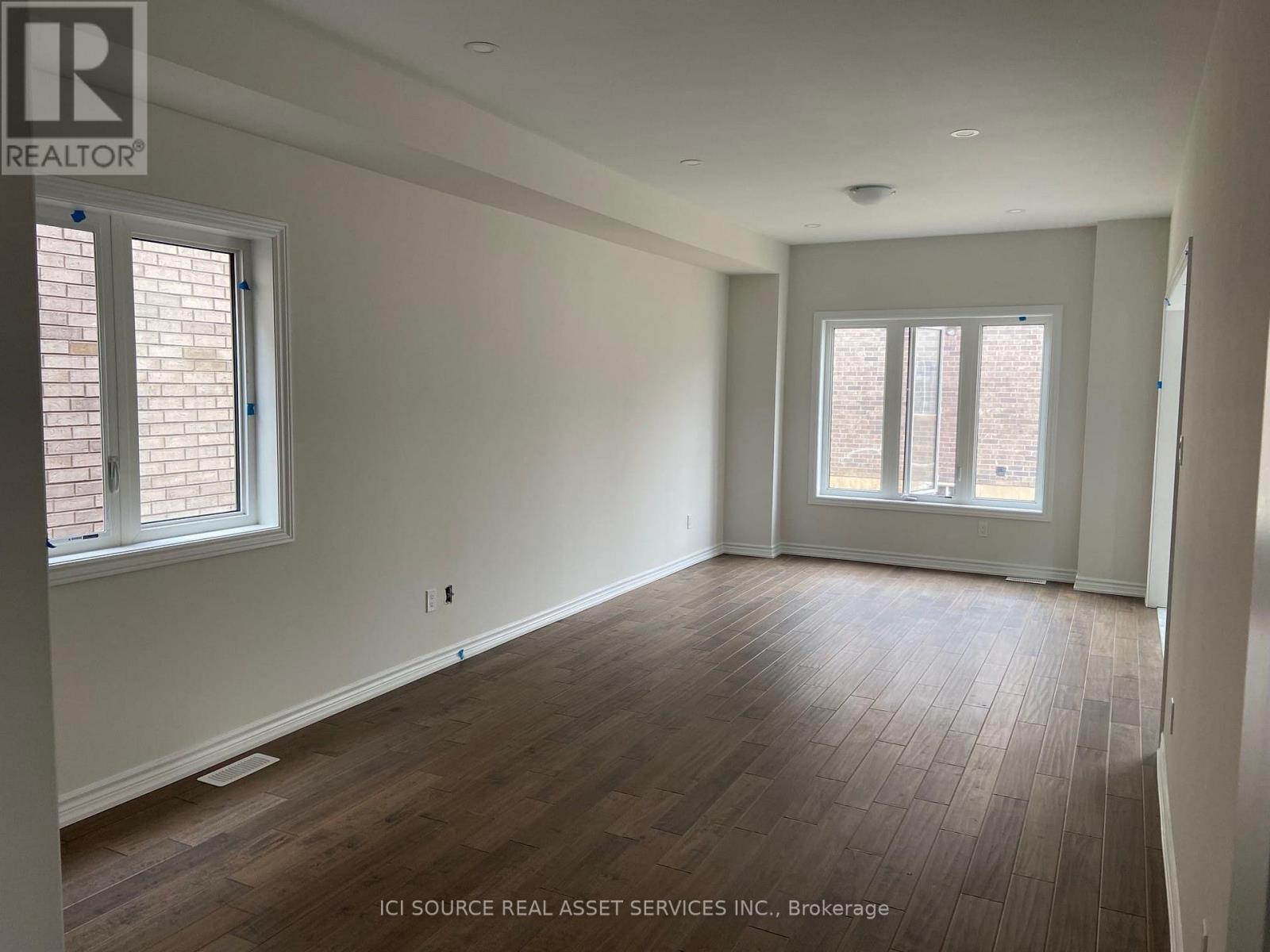 A room with wooden flooring and two windows.
