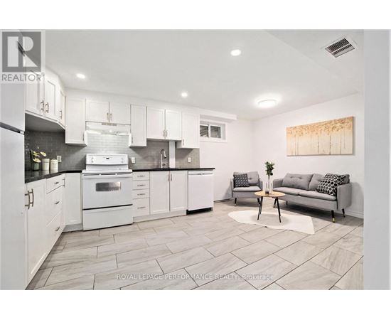 A modern kitchen with white cabinets and a grey sofa.