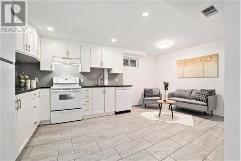 A modern kitchen with white cabinets and a grey sofa.