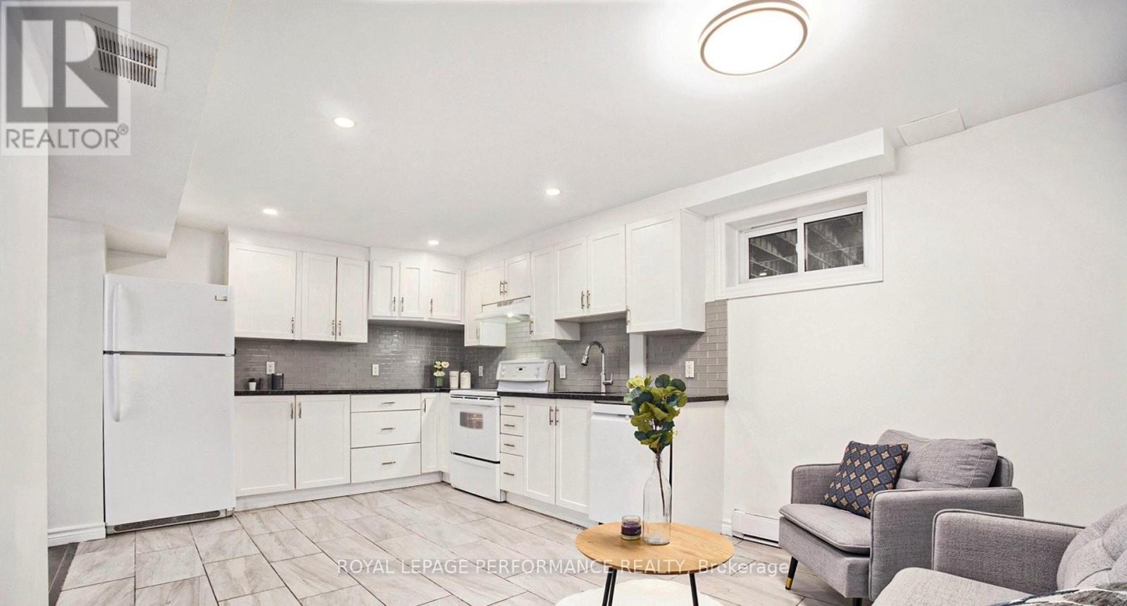 A well-lit kitchen with white appliances and a dining area with a grey couch and a wooden table.