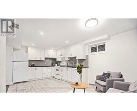 A well-lit kitchen with white appliances and a dining area with a grey couch and a wooden table.