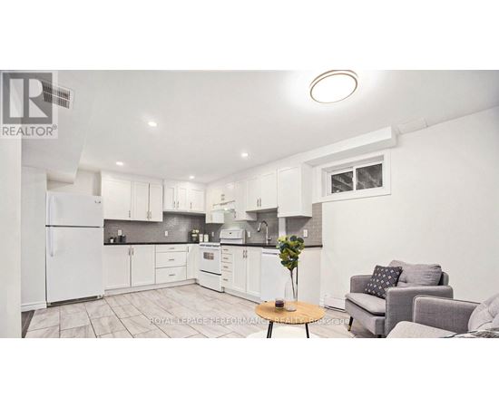 A well-lit kitchen with white appliances and a dining area with a grey couch and a wooden table.