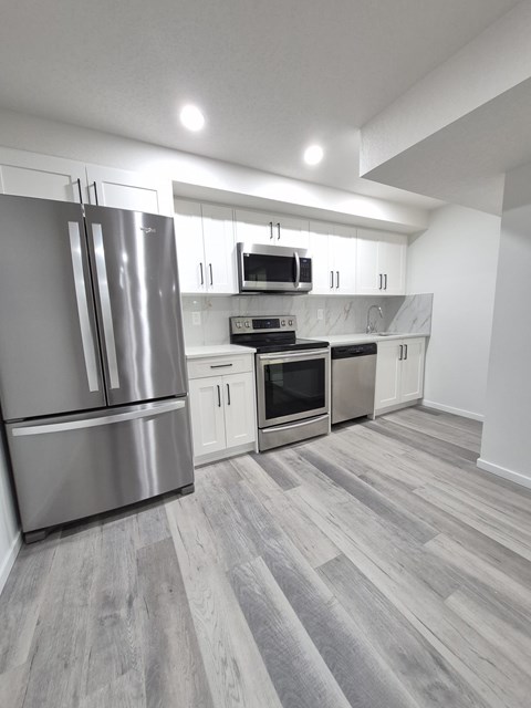 A modern kitchen with stainless steel appliances and wooden flooring.