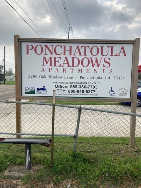 A sign for Ponchatoula Meadows Apartments sits in front of a fence.