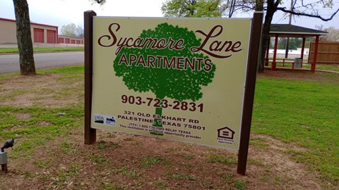 A sign for Sycamore Lane Apartments is displayed in a grassy area.