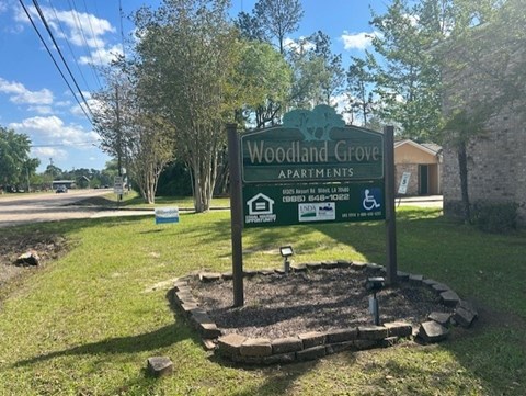 A sign for Woodland Grove Apartments stands in a grassy area.