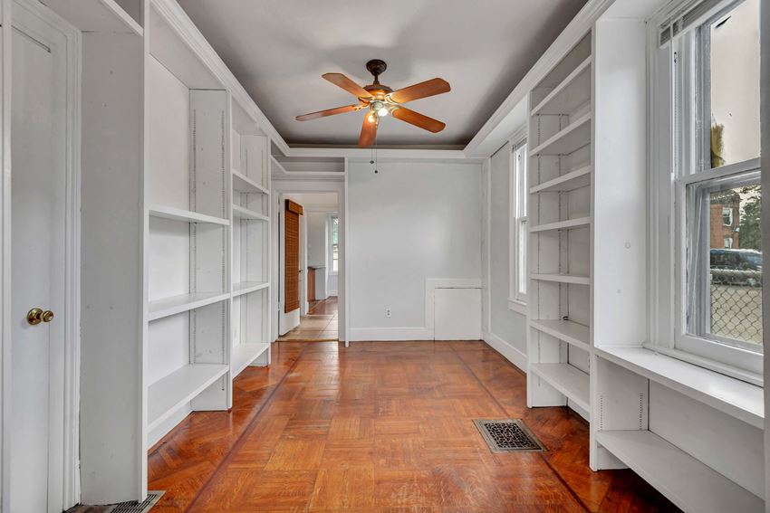 a long hallway with white shelves and a ceiling fan