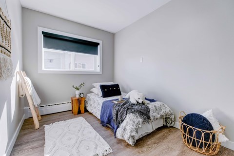 A bedroom with a bed, a basket, and a window.