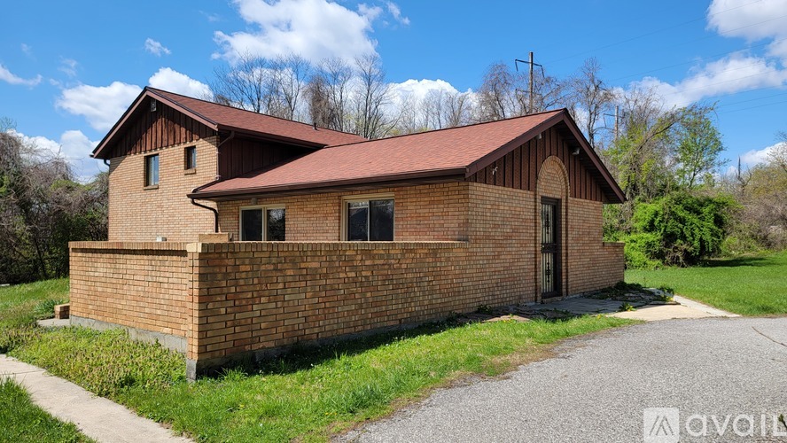 A brick house with a brown roof and a gravel driveway in front.
