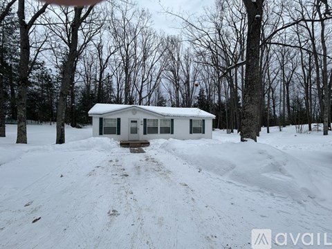 A small white house is surrounded by snow and leafless trees.