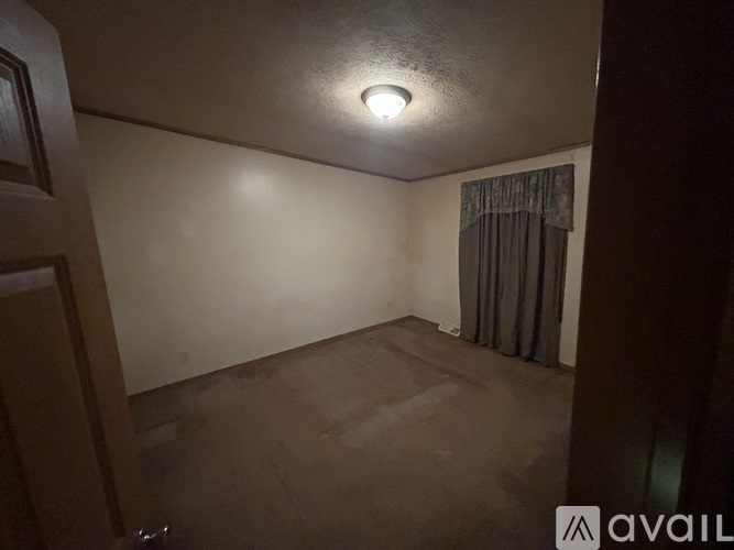 A room with a single light on the ceiling and a curtain on the window.