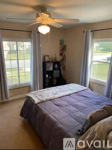 A bedroom with a bed, a ceiling fan, and a window with curtains.