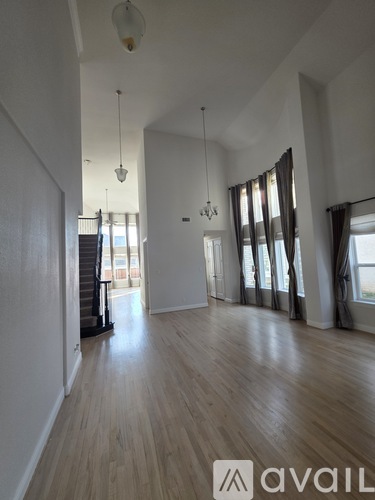 A spacious room with wooden floors and a large window with curtains.