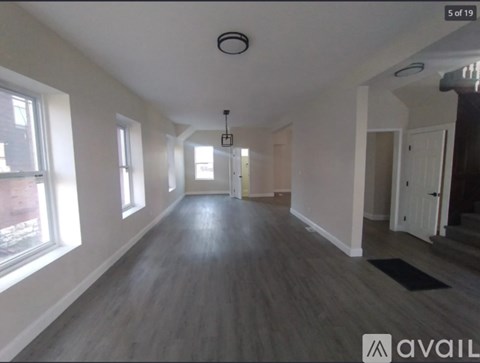 A spacious room with wooden floors and a large window on the left side.