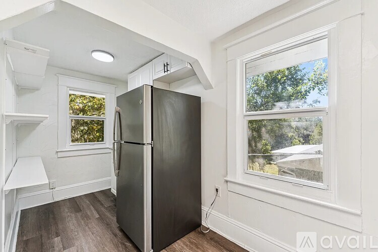 A black refrigerator in a kitchen with a window showing trees outside.