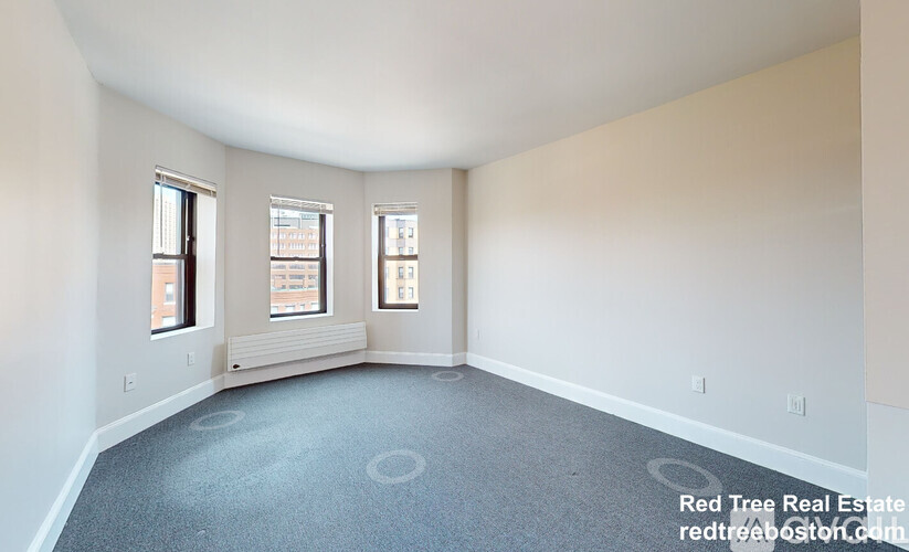 A room with a grey carpet and three windows.