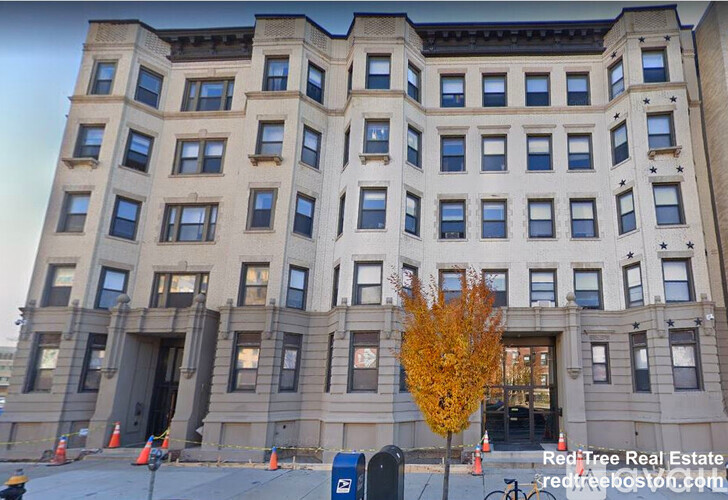 A large, beige building with many windows and a tree in front of it.