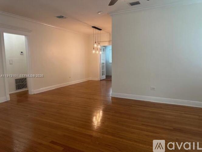 A spacious room with wooden flooring and a chandelier.