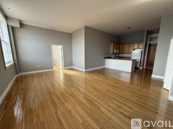 A spacious room with wooden flooring and a kitchen area in the background.
