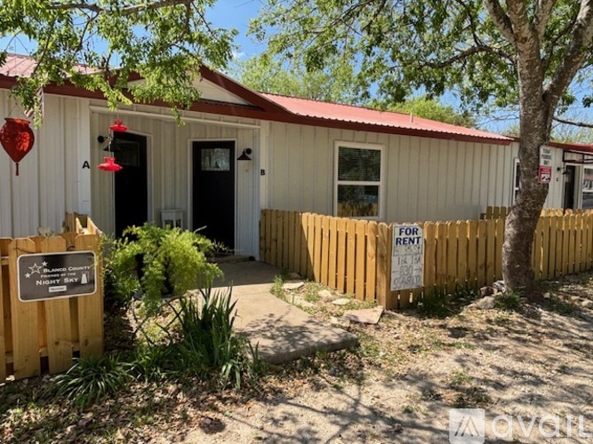 A small white building with a red roof and a wooden fence in front of it.