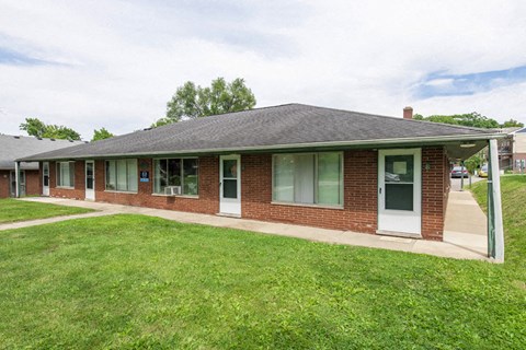 the front of a brick house with a lawn and a sidewalk