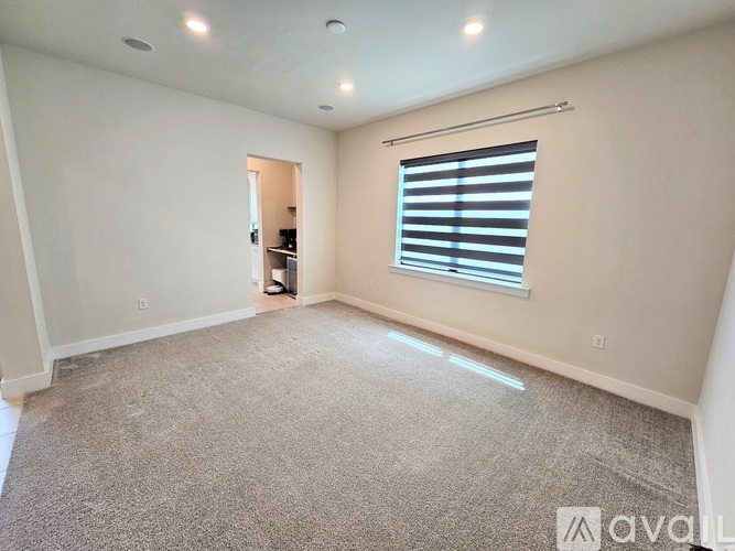 A spacious room with a carpeted floor and a window with blinds.