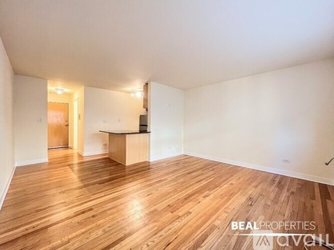 A spacious room with wooden flooring and a kitchenette.