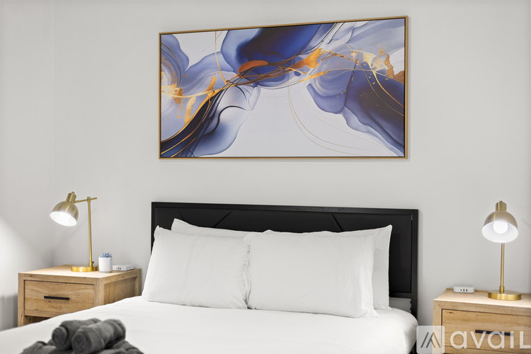 A bedroom with a large painting above the bed and two lamps on either side of the bed.