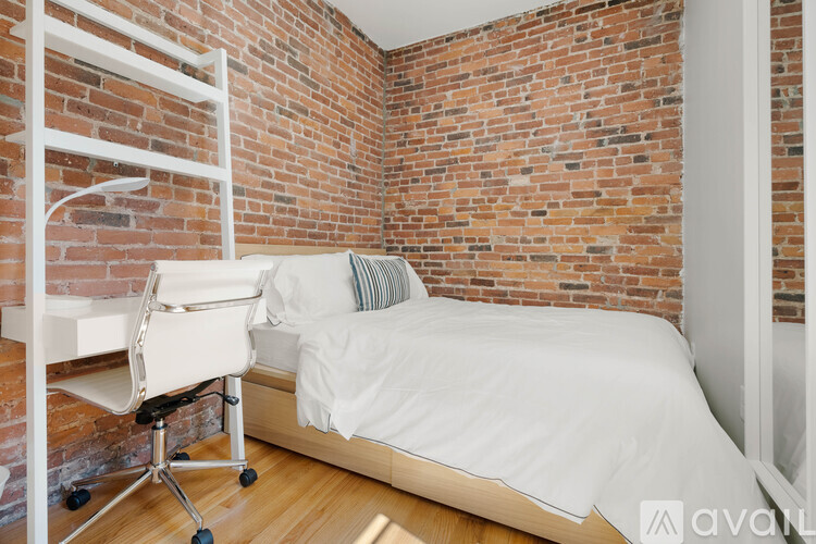 A bedroom with a bed, chair, and brick wall.