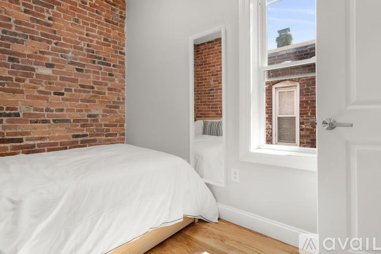 A bedroom with a white bed and a brick wall.